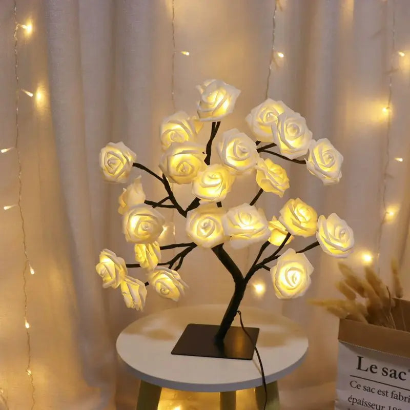 Warm white LED rose flower tree lamp with realistic rose-shaped lights, set on a black base, illuminating a cozy and romantic ambiance against a curtain backdrop with additional fairy lights, ideal for bedroom or living room decor