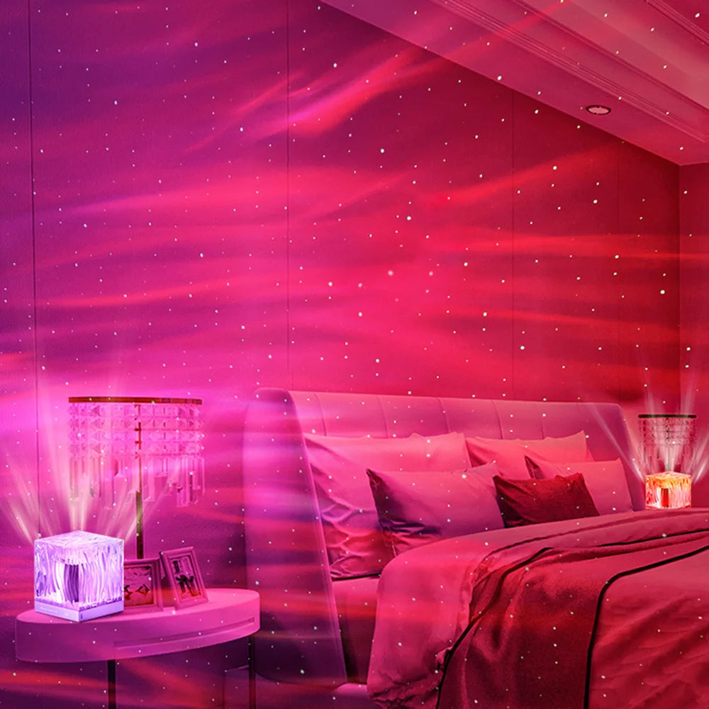 Romantic red and pink LED projection lamp creating soft, starry light patterns on bedroom walls. The cube-shaped lamp sits on a nightstand, illuminating the room with a warm, cozy glow. Paired with an elegant crystal lamp and framed photos, this setup enhances the relaxing and intimate ambiance, perfect for a dreamy night setting.