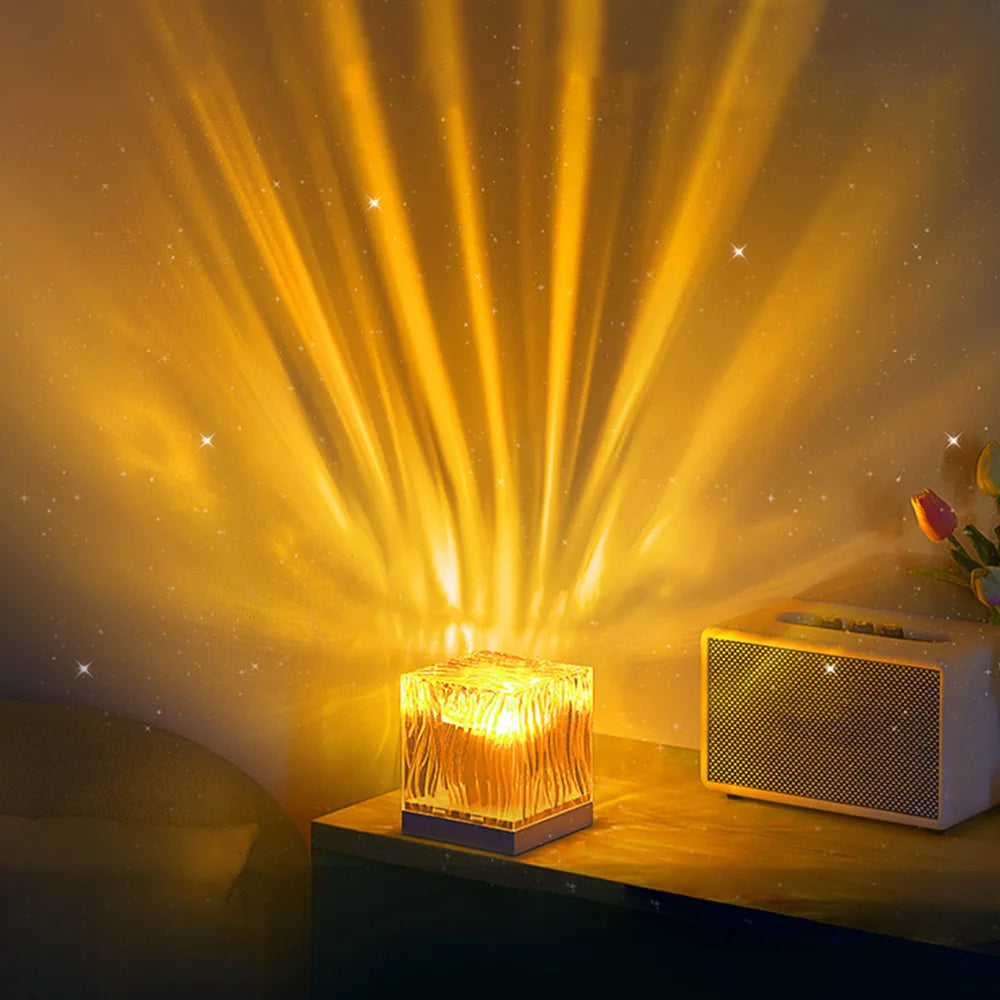 Golden LED cube lamp with a textured, wave-like design, casting a warm, radiant glow across the wall, creating a dramatic sunburst effect. Placed on a bedside table with a retro-style speaker and tulips in the background, perfect for enhancing a cozy, ambient setting in modern home decor.