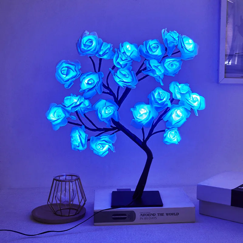 Blue LED rose flower lamp with a black tree-style base, illuminating a room with a soft blue glow. The unique lamp sits on a book titled 'Around the World in 80 Days' on a minimalistic white surface, adding a touch of creative decor. The vibrant blue roses offer a serene and calming ambiance, perfect for unique home lighting or nightstand decor.