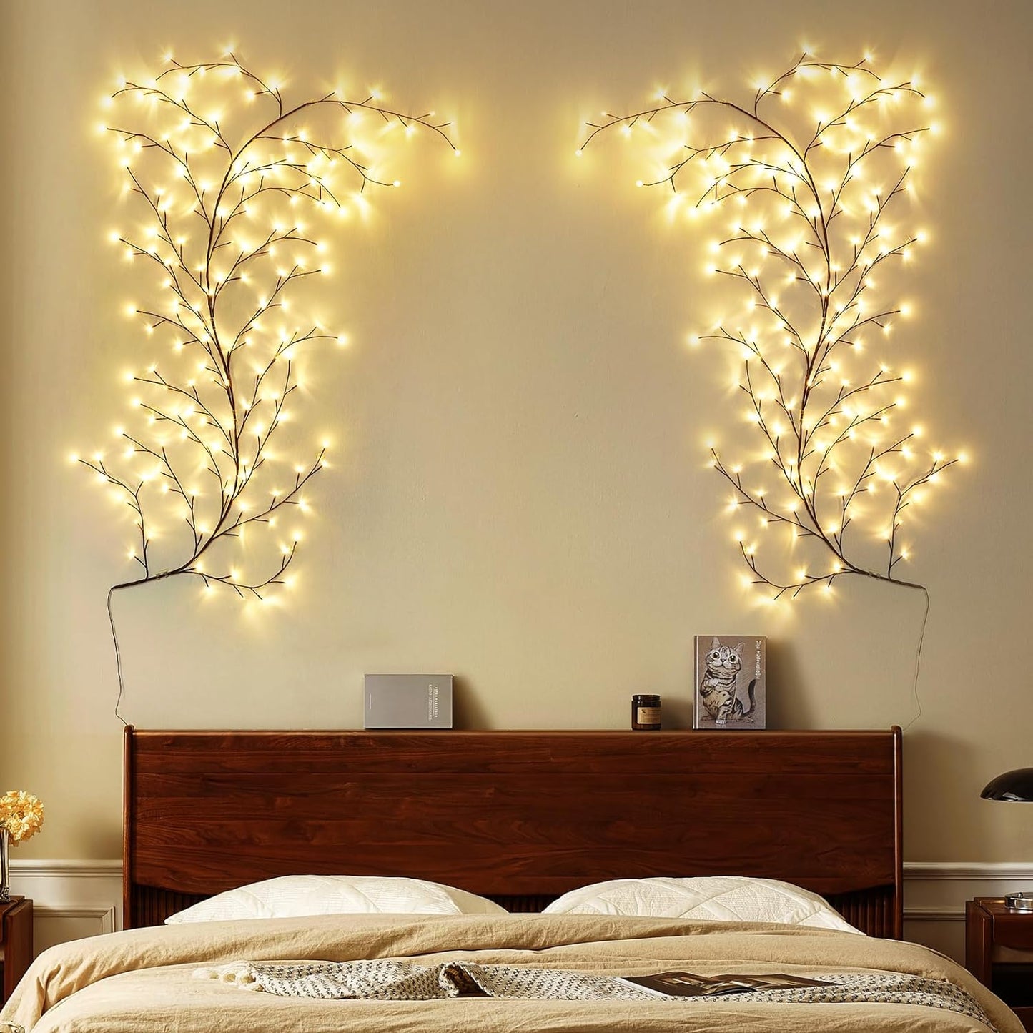 a serene bedroom setting with wall-mounted, tree branch-style LED lights on both sides above the headboard, creating a symmetrical and natural ambiance. The lights resemble gentle, glowing branches reaching upwards, enhancing the cozy and warm feeling of the room. The minimalistic decor and wooden headboard complement the soft lighting, adding to the peaceful and inviting atmosphere. This setup would be ideal for anyone looking to add a subtle, nature-inspired touch to their bedroom