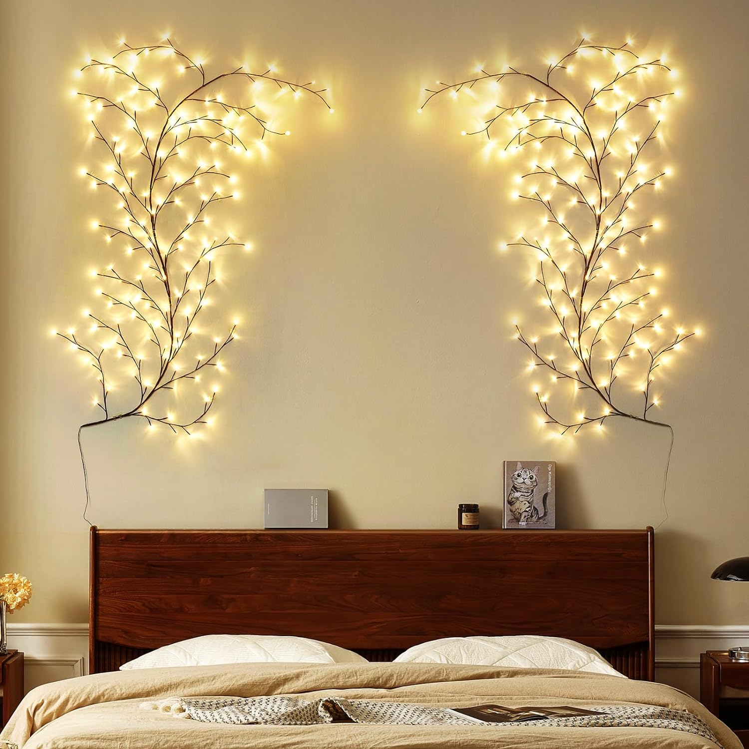 a serene bedroom setting with wall-mounted, tree branch-style LED lights on both sides above the headboard, creating a symmetrical and natural ambiance. The lights resemble gentle, glowing branches reaching upwards, enhancing the cozy and warm feeling of the room. The minimalistic decor and wooden headboard complement the soft lighting, adding to the peaceful and inviting atmosphere. This setup would be ideal for anyone looking to add a subtle, nature-inspired touch to their bedroom