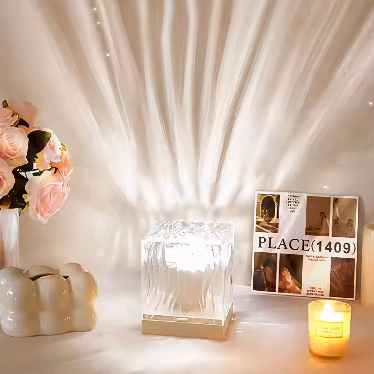 Elegant white LED cube lamp with textured glass, emitting soft ambient light that creates a radiant pattern on the wall. Styled with delicate pink roses, a white ceramic vase, a decorative candle, and a modern magazine, perfect for minimalist home decor or cozy bedroom ambiance.