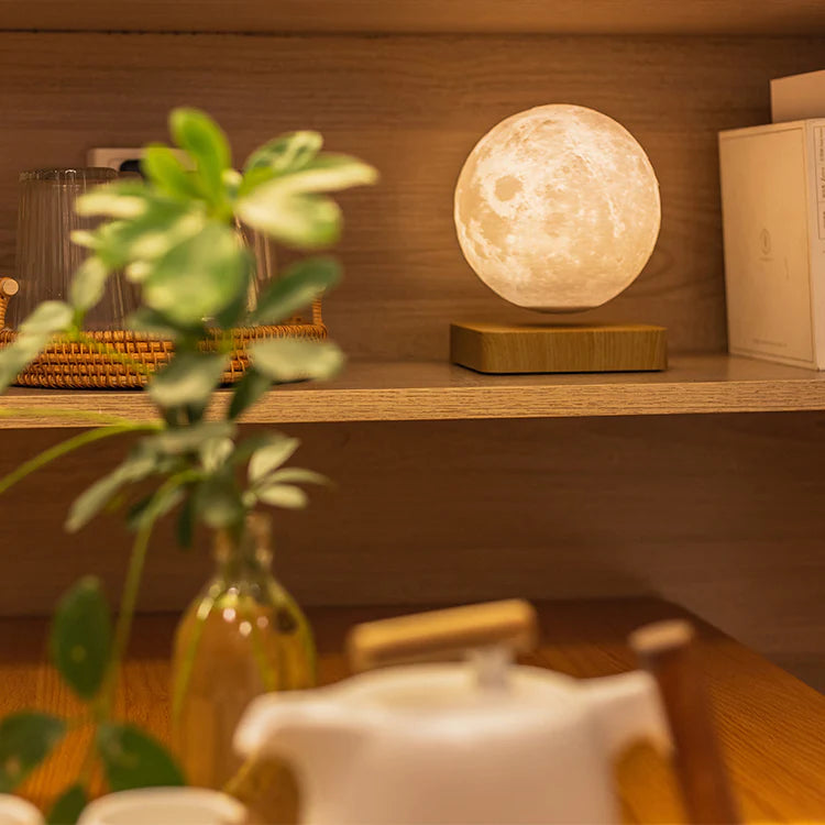 A levitating moon lamp with a lifelike lunar surface, softly glowing on a wooden shelf. The floating orb adds a serene and enchanting ambiance to the cozy setting, nestled among greenery and decorative items for a warm, nature-inspired decor.