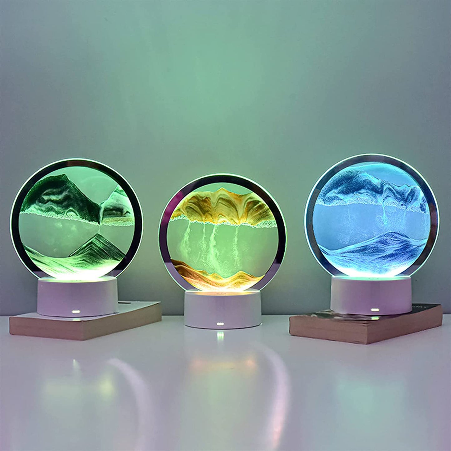 A trio of LED sand art lamps displaying dynamic landscapes in green, yellow, and blue hues. Each lamp showcases shifting sand patterns that create serene mountainous scenes, enhanced by the ambient glow of the LED lights. Perfect for adding a calming, artistic touch to any room.