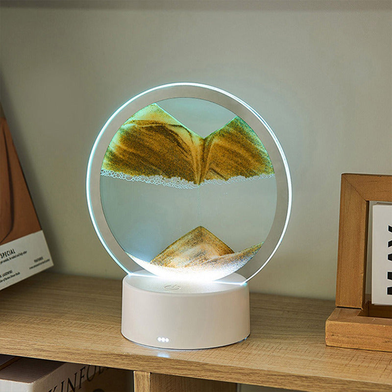 A circular LED sand art lamp featuring golden sand forming a serene mountain landscape, encased in a sleek frame. This tabletop decor piece illuminates gently, creating a calming ambiance ideal for desks or shelves.