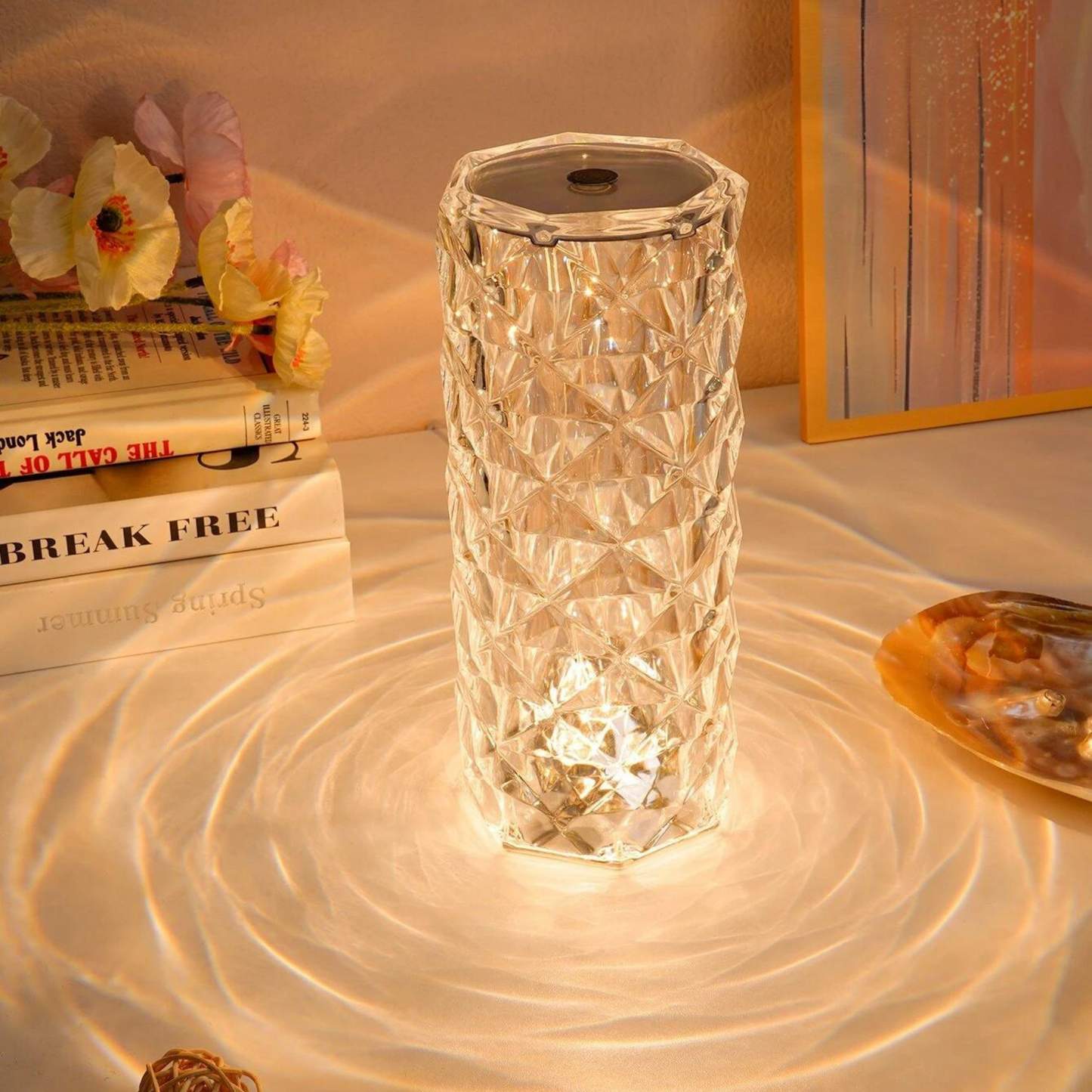 A hexagonal crystal LED lamp with a diamond-cut surface, emitting a warm, ambient glow. The intricate crystal pattern reflects light in circular ripples, casting beautiful, wavy patterns on the surface below. Surrounded by books and decorative accents, this lamp serves as an elegant, eye-catching centerpiece, enhancing any modern or classic decor with a touch of sophistication and warm illumination.