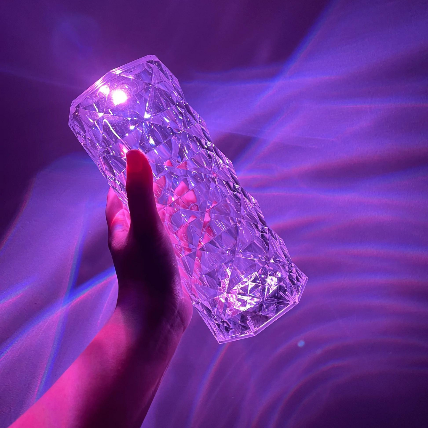 A handheld crystal LED lamp with a hexagonal, diamond-cut design, emitting a vivid purple light. The crystal surface reflects light in dynamic, wavy patterns, creating an ethereal glow on the surrounding area. The lamp's intricate texture and vibrant hue combine to form a mesmerizing visual effect, perfect for adding an ambient and artistic touch to any space.