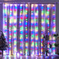 Vibrant multicolor LED curtain lights draped over sheer curtains, creating a festive and joyful atmosphere. The lights display a mix of red, green, blue, and yellow, adding a lively, colorful touch to the room. Decorated with a small Christmas tree and a bookshelf adorned with plants and decor items, this setup is perfect for holiday celebrations or creating a playful ambiance.