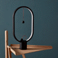 A modern magnetic balance lamp featuring a sleek, oval design with a unique suspension system. This lamp lights up when the two spherical magnetic balls align in the center, creating a visually intriguing and minimalist effect. Set against a dark teal wall, this elegant piece blends function and art, ideal for contemporary decor and a subtle lighting experience. The black frame and base add a sophisticated touch, while the red strings give a hint of color contrast, making it a perfect choice for stylish wor