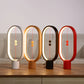 A set of four minimalist magnetic balance lamps in varying finishes — white, natural wood, black, and red — each featuring an oval frame with a warm LED light strip along the inner edge. Positioned on a wooden table against a neutral backdrop, these lamps create a cohesive yet vibrant display. Each lamp has two magnetic spheres suspended on a red cord, floating in the center when aligned to switch on the light. This stylish collection showcases modern design, adding both functional lighting and an artistic 