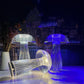 Three crystal mushroom-shaped LED lamps arranged on a surface against a cityscape backdrop, with two upright and one laying down. The clear, ribbed design of each lamp amplifies and refracts the light, casting a luminous glow in varying shades, including cool blues and warm whites. These lamps create a stylish, contemporary atmosphere with reflections and ambient lighting, perfect for modern decor or a futuristic aesthetic.