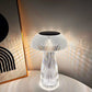 A sophisticated crystal mushroom lamp with a ribbed texture emits a radiant glow, casting intricate light patterns on the surrounding wall. Positioned beside a framed abstract artwork, this lamp enhances the modern decor with its soft illumination and elegant design. The sleek black top contrasts beautifully with the transparent body, creating a refined ambiance. This lamp serves as a striking centerpiece, perfect for elevating the aesthetic appeal of contemporary interiors.