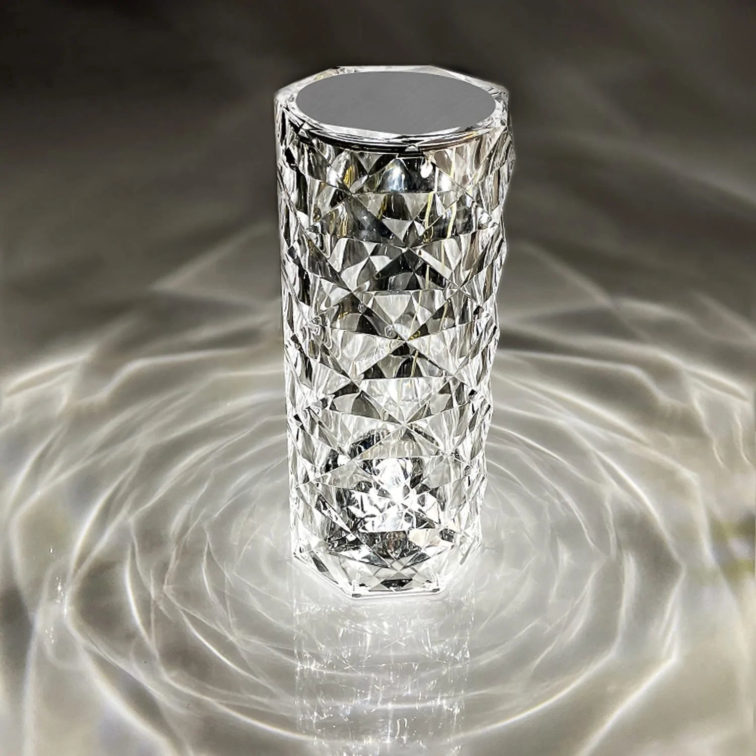 A crystal LED lamp with a tall, diamond-cut design, casting mesmerizing light patterns in concentric circles around it. The faceted surface of the lamp reflects light beautifully, creating a sophisticated ambiance with an almost water-like ripple effect. This elegant, modern lamp adds a touch of luxury and visual interest to any space, enhancing the room's decor with its unique and eye-catching lighting.






