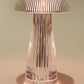 A sleek crystal mushroom LED lamp with a ribbed, transparent structure, emitting a soft, warm light. The lamp’s elegant design features a fluted stem and a rounded, dome-like top, creating a modern and sophisticated lighting piece that casts gentle reflections on the surrounding surface. This versatile decor item is ideal for adding ambient lighting to any contemporary space, blending both functionality and aesthetic appeal.