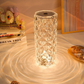 A hexagonal crystal LED lamp with a diamond-cut surface, emitting a warm, ambient glow. The intricate crystal pattern reflects light in circular ripples, casting beautiful, wavy patterns on the surface below. Surrounded by books and decorative accents, this lamp serves as an elegant, eye-catching centerpiece, enhancing any modern or classic decor with a touch of sophistication and warm illumination.