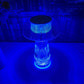 A crystal mushroom lamp bathed in a vibrant blue glow illuminates the room with an enchanting, futuristic ambiance. The ribbed glass structure enhances the intensity of the light, creating a striking ripple effect on the surrounding surface. This unique lighting choice exudes a captivating, modern appeal, ideal for adding a touch of bold elegance to any space. Perfect for night-time decor, this lamp transforms the atmosphere with its deep, mesmerizing blue radiance.