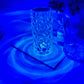 A crystal LED lamp with a hexagonal, diamond-cut design illuminated in a vibrant blue hue. The faceted crystal surface reflects light, creating captivating, ripple-like patterns that spread outwards, adding a soothing ambiance to the space. Perfect as a statement piece for modern decor, this lamp’s unique shape and striking blue illumination bring an artistic and luxurious touch to any room.
